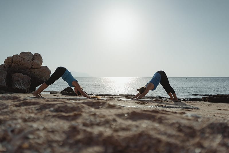a couple of people doing yoga on a beach, with the sky, water, and ground in the background
